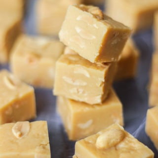 Overhead angled photo of pile of microwave peanut butter fudge cubes with salted peanuts on top on grey background.