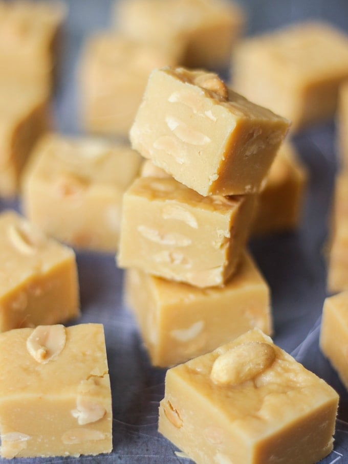 Overhead angled photo of pile of microwave peanut butter fudge cubes with salted peanuts on top on grey background.