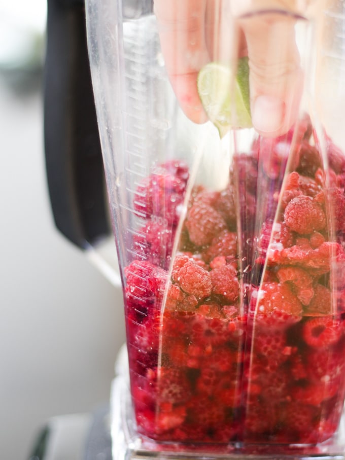 Frozen raspberries in a blender with lime being squeezed in for Raspberry Gin Frozen Cocktail Recipe.