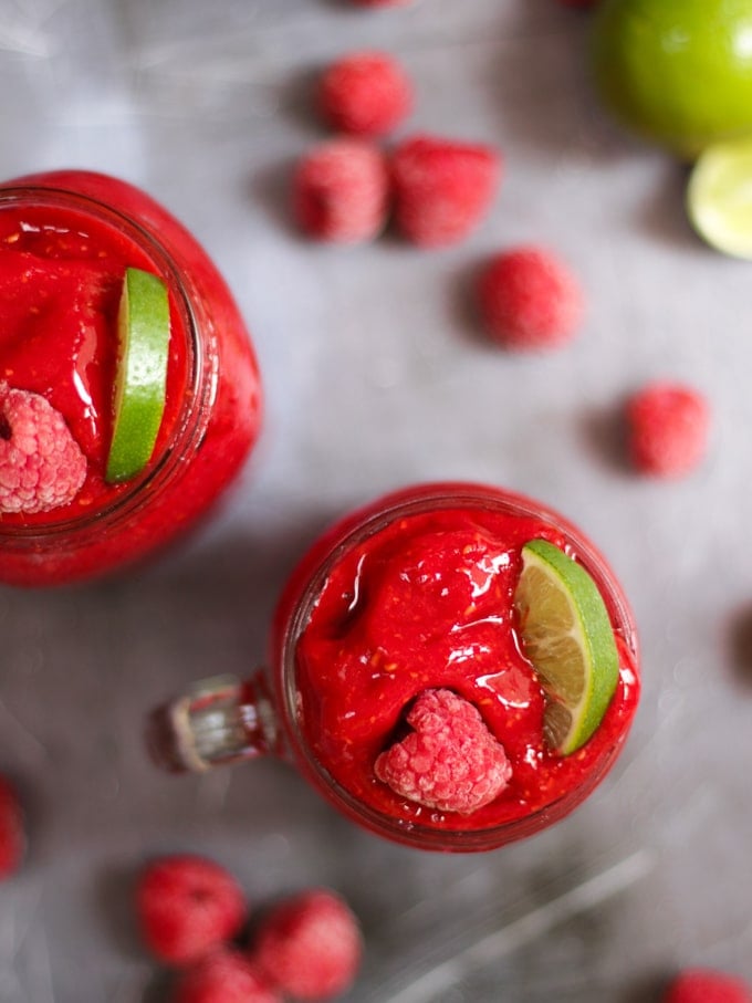 Overhead photo of raspberry gin frozen cocktails. Adult slushies tipped with raspberries and lime wedges on a grey background.