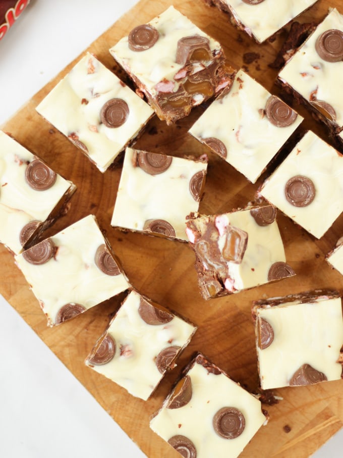 Overhead photo os Rolo Rocky Road Squares made with Roll Rocky Road Recipe, topped with white chocolate and Rolls on a wooden board.