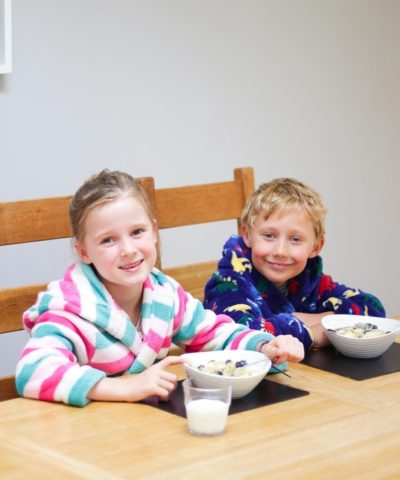 Girl and boy in dressing gowns as table eating porridge.
