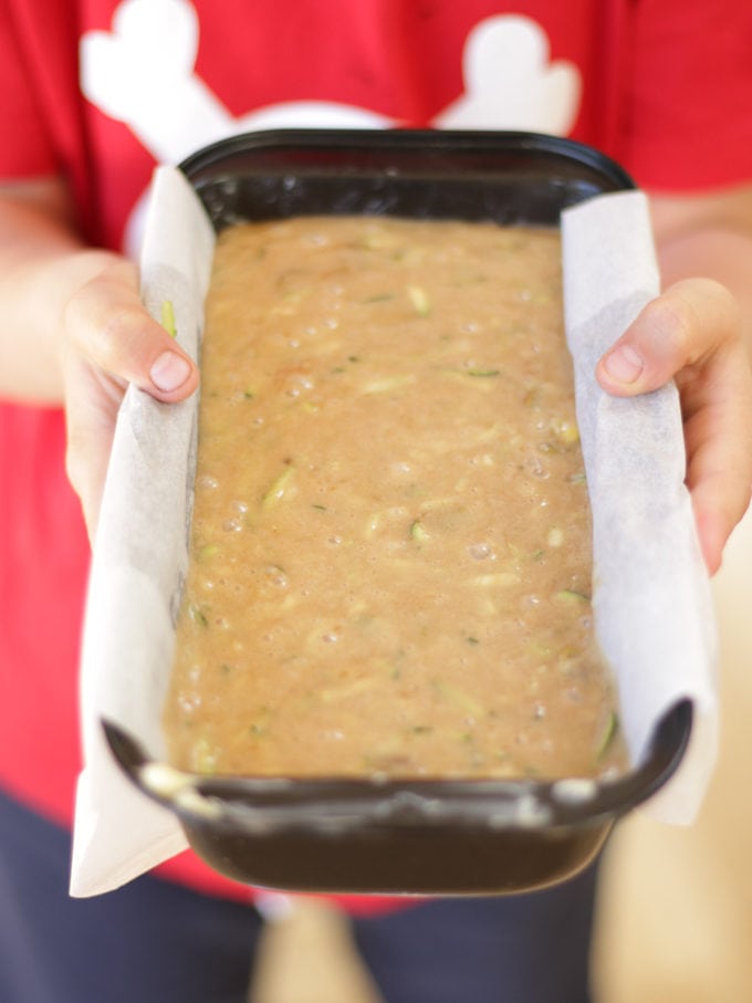 Child holding a loaf tin with courgette cake recipe mixture in.