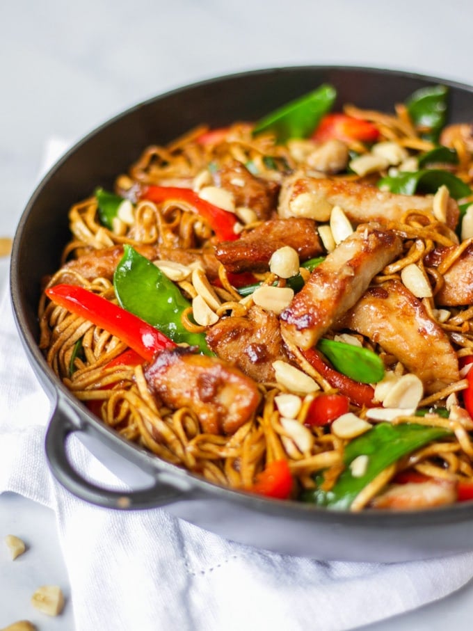 Side angle photo of pork stir fry recipe with noodles, pork, red peppers and mange tout and peanuts.