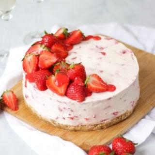 Side angle photo of strawberry cheesecake top with halves strawberries and strawberry coulis drizzle on wooden board and white marble background