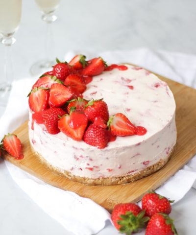 Side angle photo of strawberry cheesecake top with halves strawberries and strawberry coulis drizzle on wooden board and white marble background