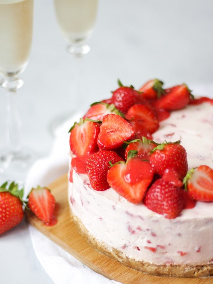 Side angle photo of strawberry cheesecake top with halves strawberries and strawberry coulis drizzle on wooden board and white marble background