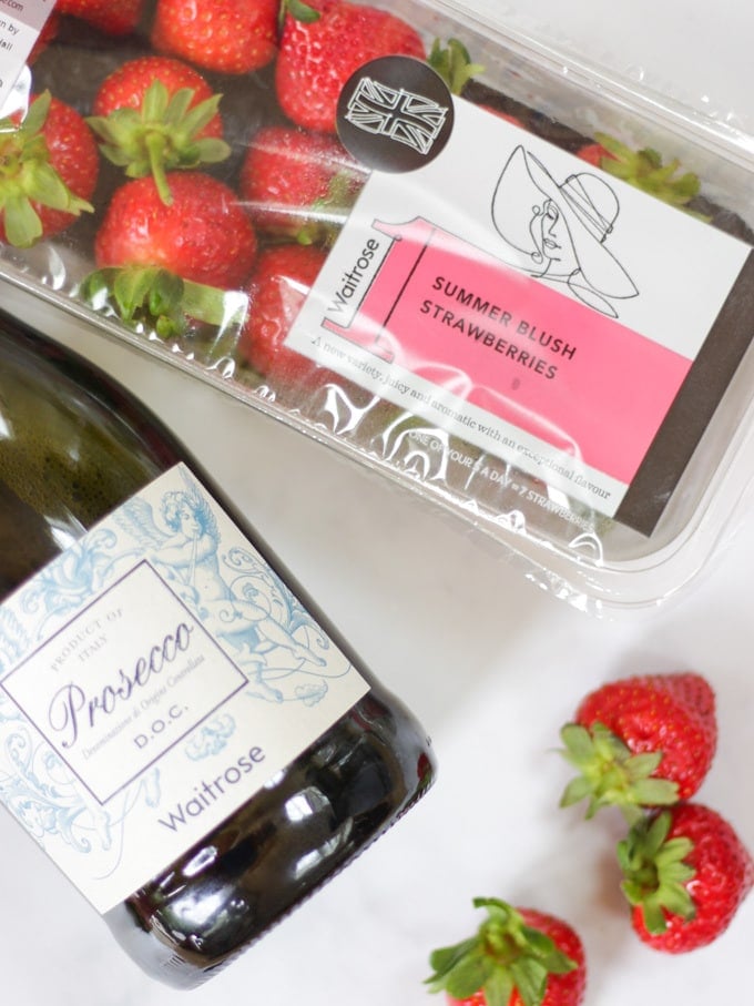 punnet of strawberries alongside a bottle of prosecco on a white background