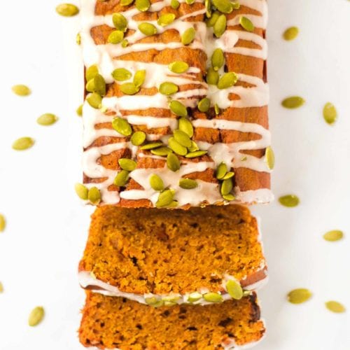 Overhead photo of a pumpkin spice loaf, pumpkin loaf cake, sprinkled with white drizzle icing and pumpkin seeds.