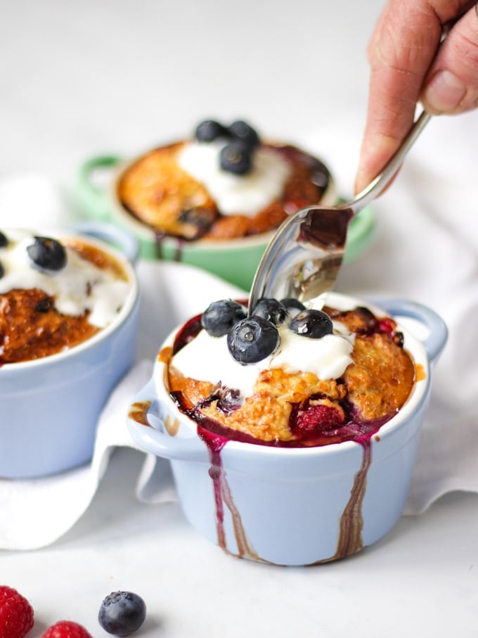 Side angle photo of baked oats in small ramekins on a white background with spoon scooping them out.