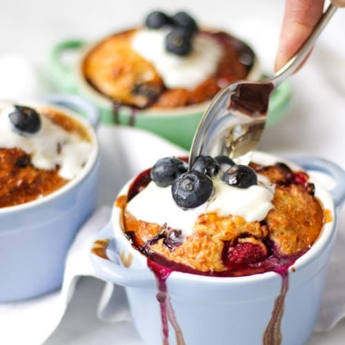 Side angle photo of baked oats in small ramekins on a white background with spoon scooping them out.