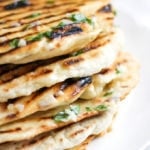 Pile stack of homemade easy three ingredient yoghurt soft flatbreads with griddle lines, garlic butter with parsley on and white plate.