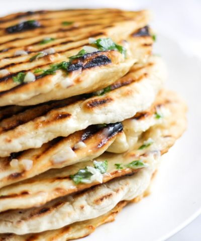 Pile stack of homemade easy three ingredient yoghurt soft flatbreads with griddle lines, garlic butter with parsley on and white plate.