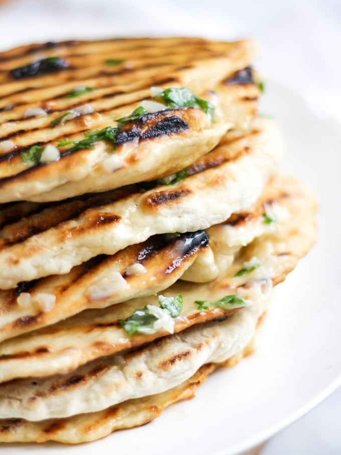 Pile of homemade soft flatbreads with garlic butter with parsley on and white plate.
