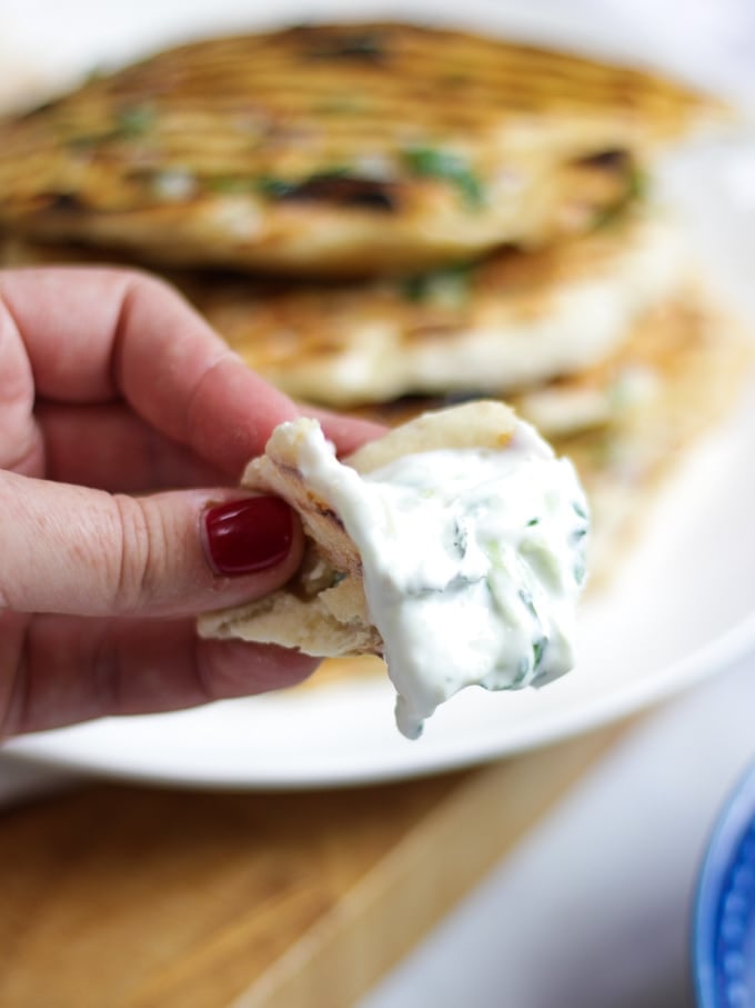 Piece of flatbread being scooped up with dip, pile of flatbreads in background. 