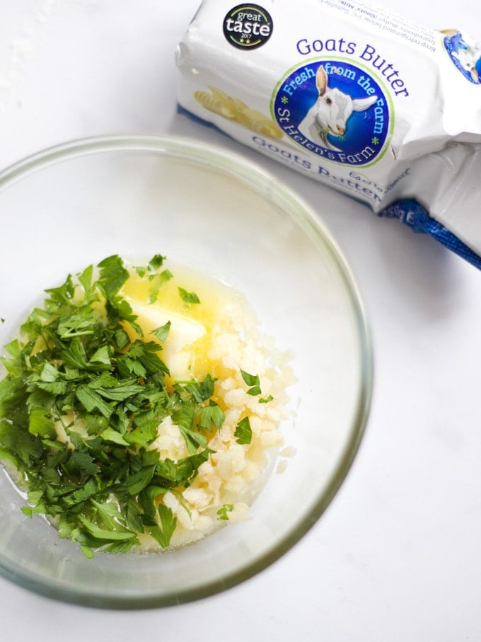 Ingredients for goats milk garlic butter with glass bowl with parsley and garlic and salt on a white background, ready to serve on flatbread. 