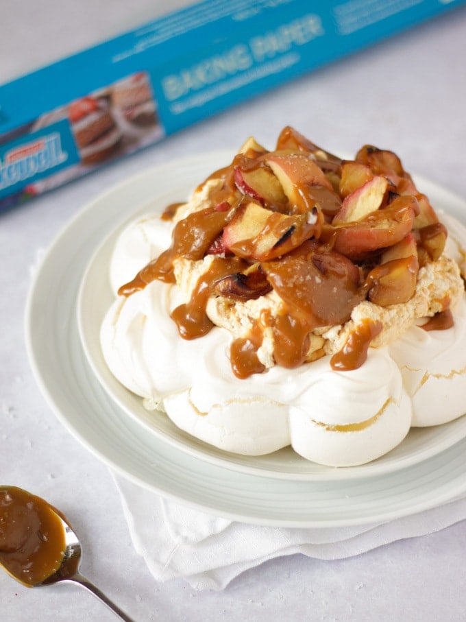 Salted caramel and apple pavlova on a white plate on white background piled with apples.