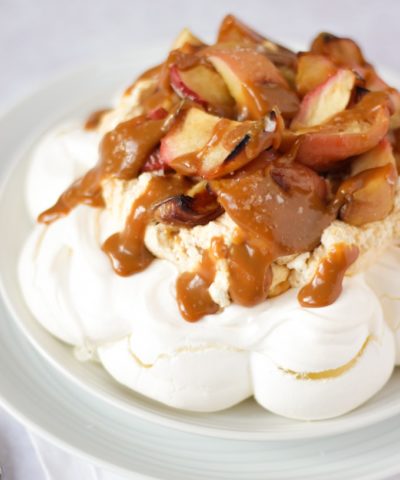 Salted caramel and apple pavlova on a white plate on white background piled with apples.