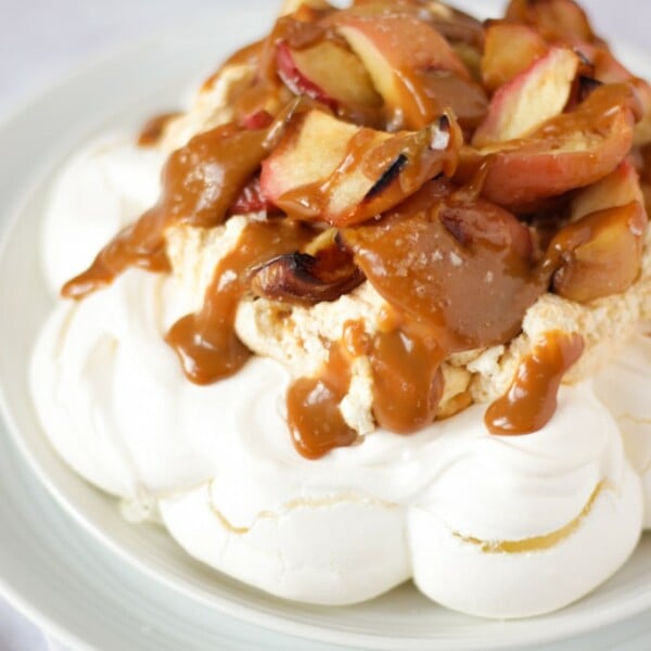 Salted caramel and apple pavlova on a white plate on white background piled with apples.