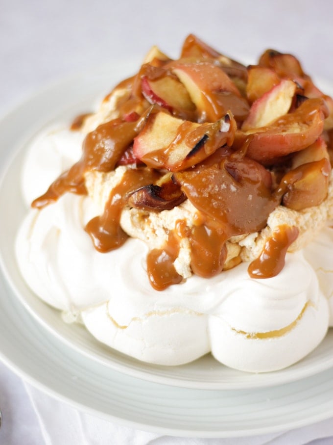 Salted caramel and apple pavlova on a white plate on white background piled with apples.