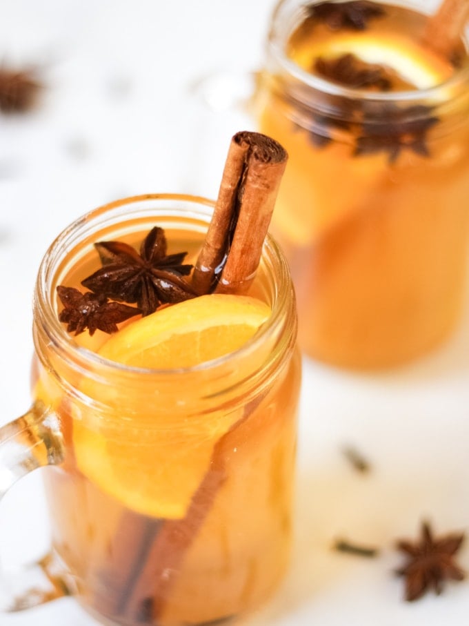 Glass mugs of spiced apple juice recipe with slices of orange, cinnamon sticks, star anise and cloves.