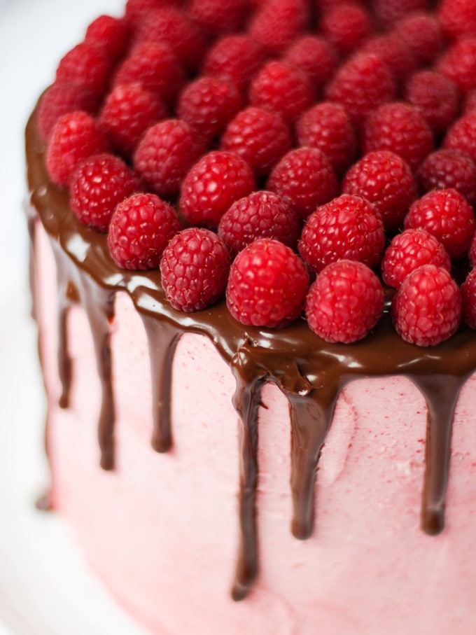 Raspberry cake on white plate on white marble background with chocolate ganache and fresh raspberries on top.