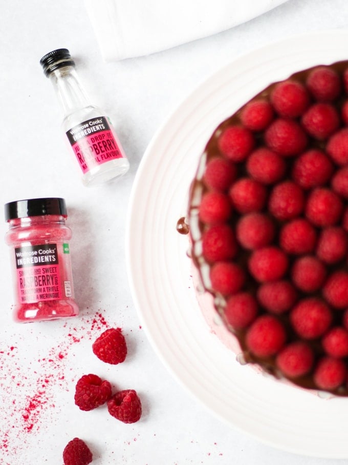Raspberry cake on white plate on white marble background with chocolate ganache and fresh raspberries on top.