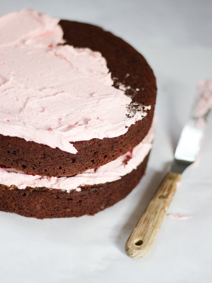 Two layers of chocolate cake sandwiched with raspberry buttercream and palette knife on the side on white marble background - showing how to decorate a raspberry cake.
