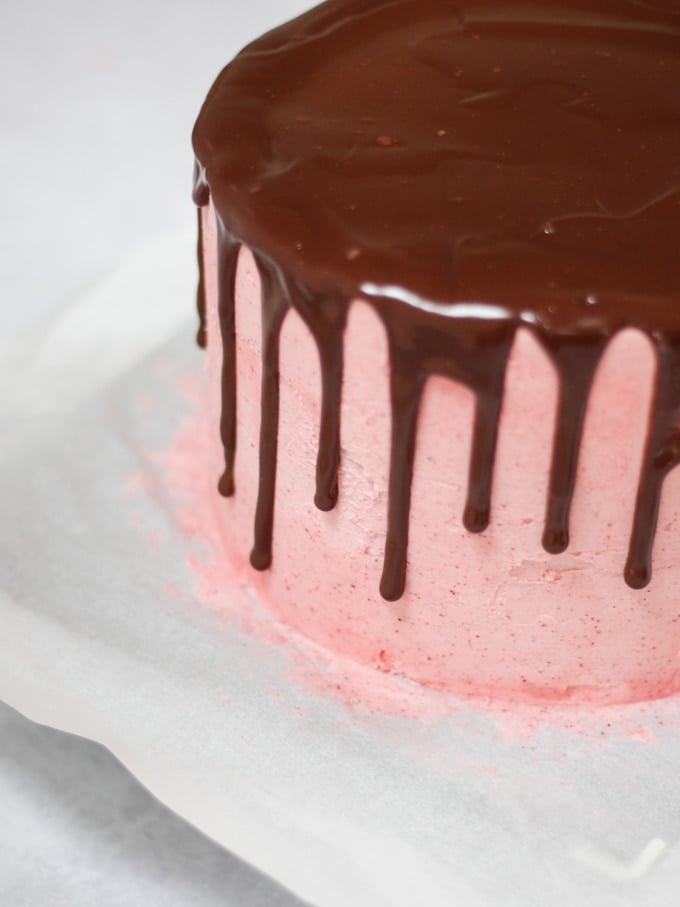 Raspberry cake coated in raspberry icing and with chocolate ganache dripping down the sides.