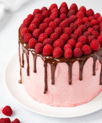Raspberry cake on white plate on white marble background with chocolate ganache and fresh raspberries on top.