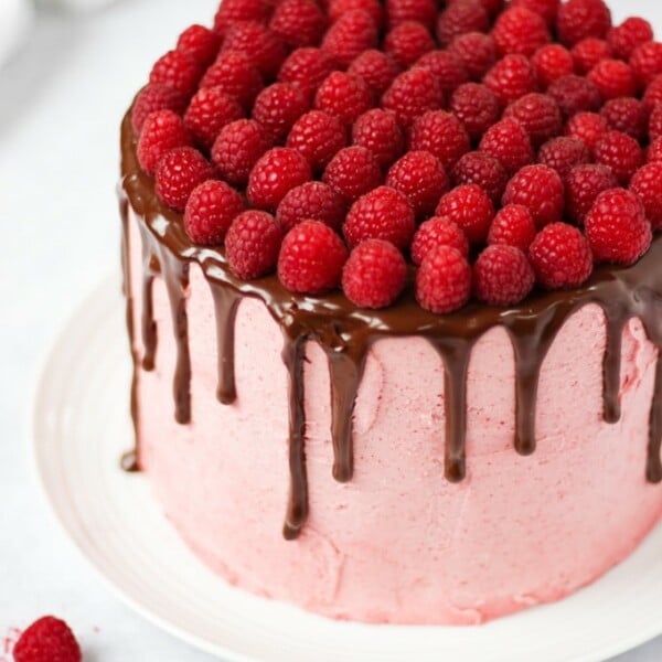 Raspberry cake on white plate on white marble background with chocolate ganache and fresh raspberries on top.