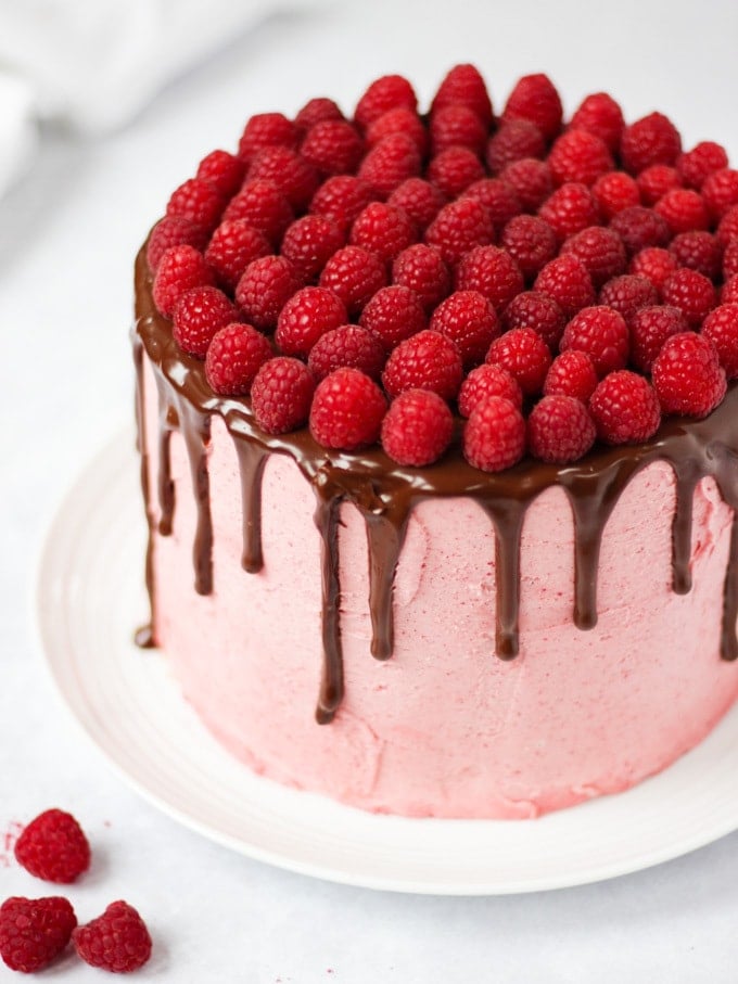 Raspberry cake on white plate on white marble background with chocolate ganache and fresh raspberries on top.