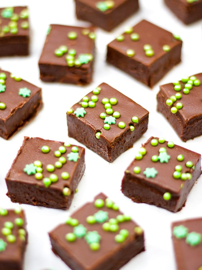 Foto em ângulo lateral de fundo de mármore branco com pedaços de bailleys fudge com salpicos verdes.