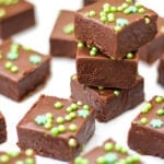 Pile of 3 pieces of easy baileys fudge and other pieces on white background with green sprinkles.