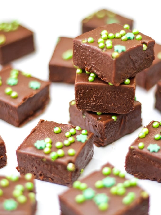 Pile of 3 pieces of easy baileys fudge and other pieces on white background with green sprinkles.