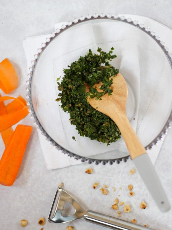 Herbs in a glass bowl with carrots on white napkin.