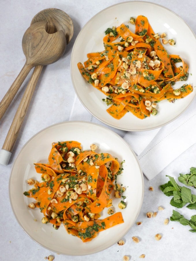 Two bowls of carrot salad with wooden salad serves and white napkin.