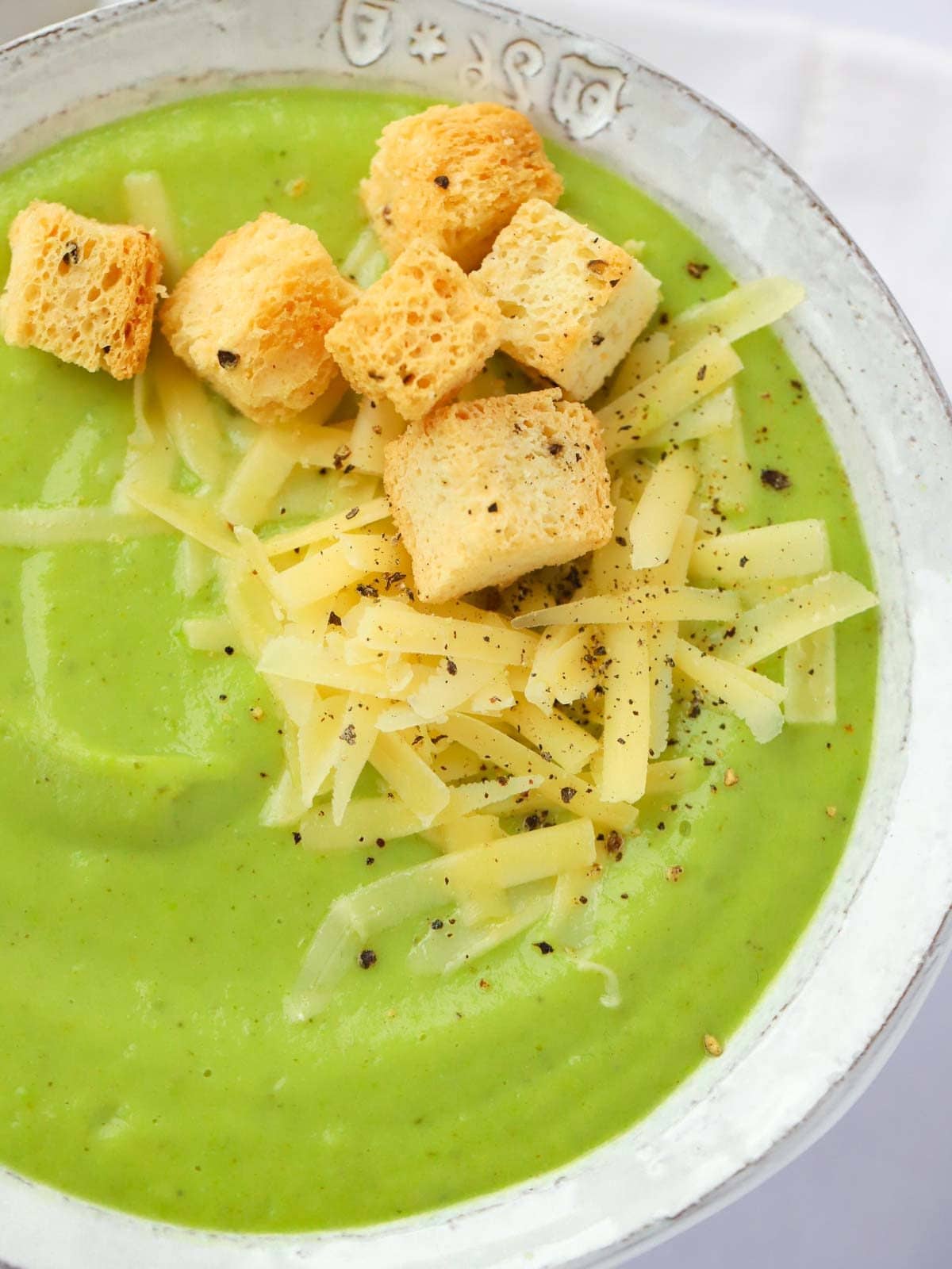 A bowl of green soup, made up of broccoli and cauliflower, with cheese and croutons on top.