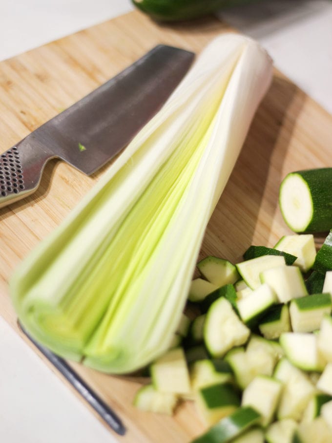 Leek cut lengthways, global knife and cubes of chopped courgette on a wooden board for courgette soup recipe.