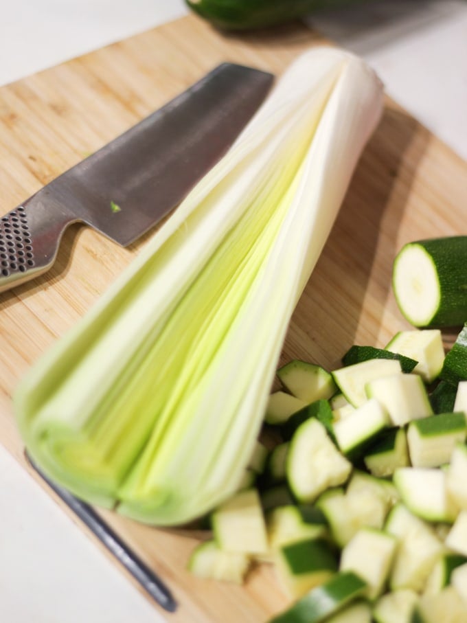 Leek cut lengthways, global knife and cubes of chopped vegetables on a wooden board for recipe.