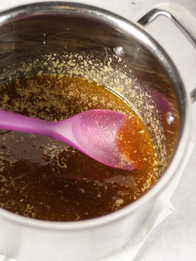 A metal saucepan with melted butter, sugar and golden syrup in with purple spatula in.