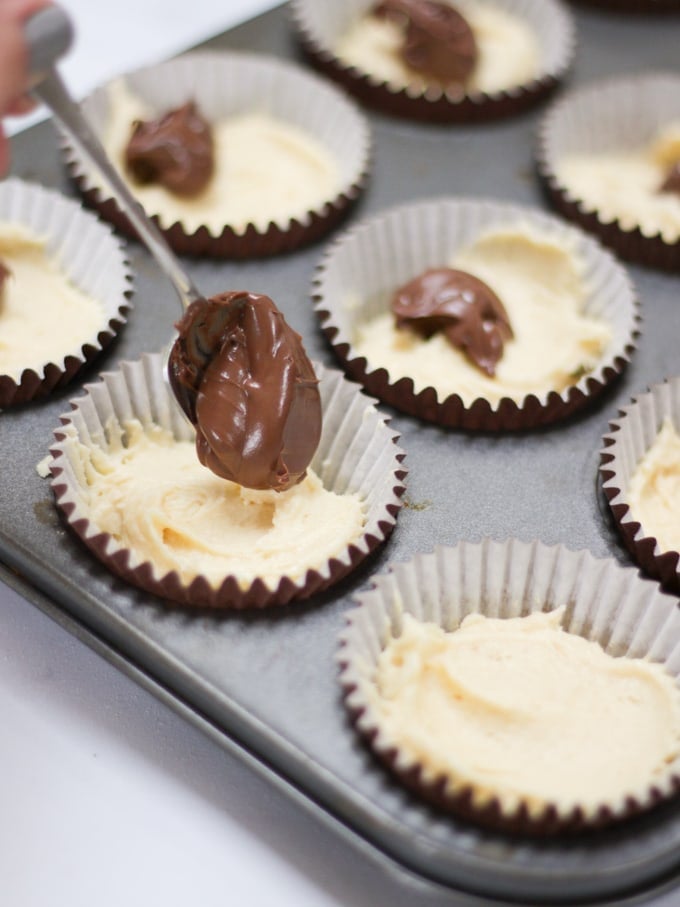 Photo of brown muffin cases in a metal muffin tray with cake batter in.