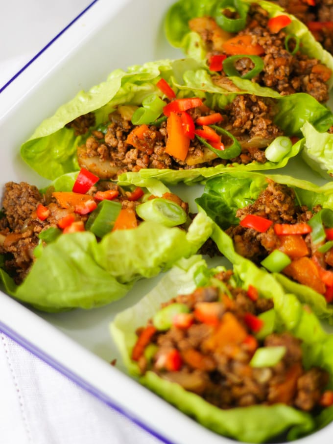 Yuk sung cooked pork mince in lettuce leaves side view in a white enamelware dish on white napkin and white marble background.