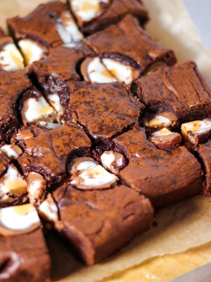 Creme Egg brownies on baking paper on a chopping board topped with cut creme eggs.