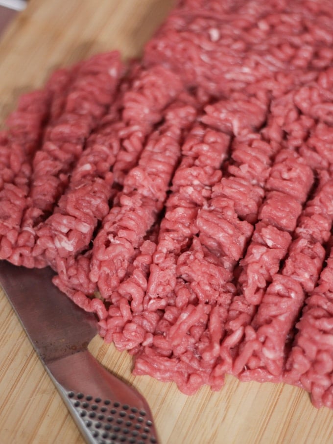 Raw minced beef being chopped on a wooden board