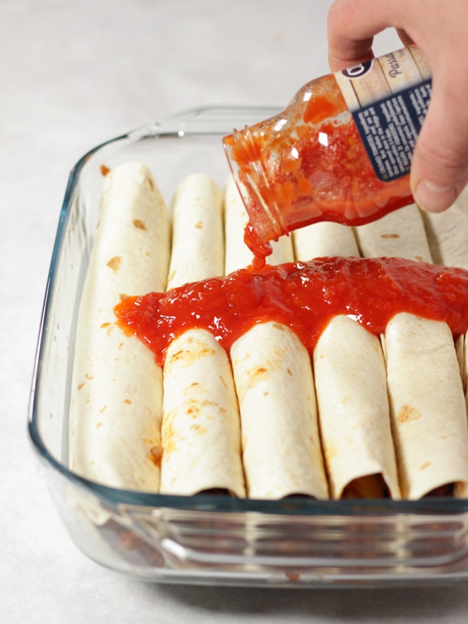Rolled uncooked wraps with tomatoes being poured over
