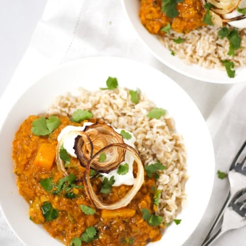 two bowls of red lentil Dahl and rice topped with onions in white bowls