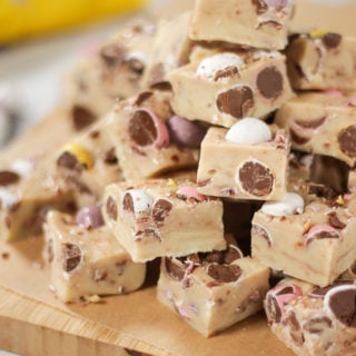 Pile of Mini Eggs Fudge for Easter cut into cubes with mini eggs showing and pack in background.
