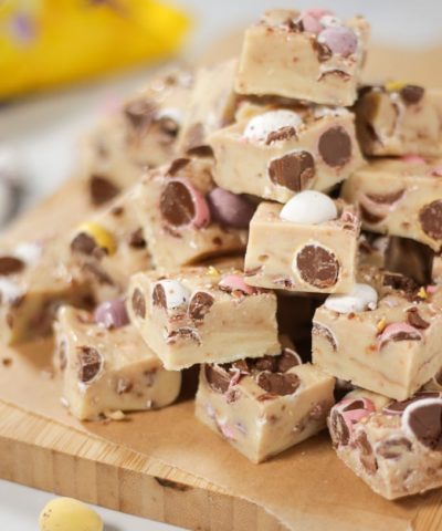 Pile of Mini Eggs Fudge for Easter cut into cubes with mini eggs showing and pack in background.