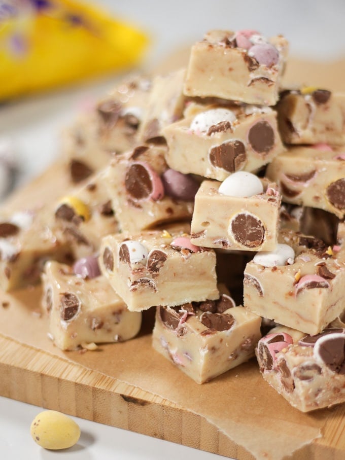 Pile of Mini Eggs Fudge for Easter cut into cubes with mini eggs showing and pack in background.